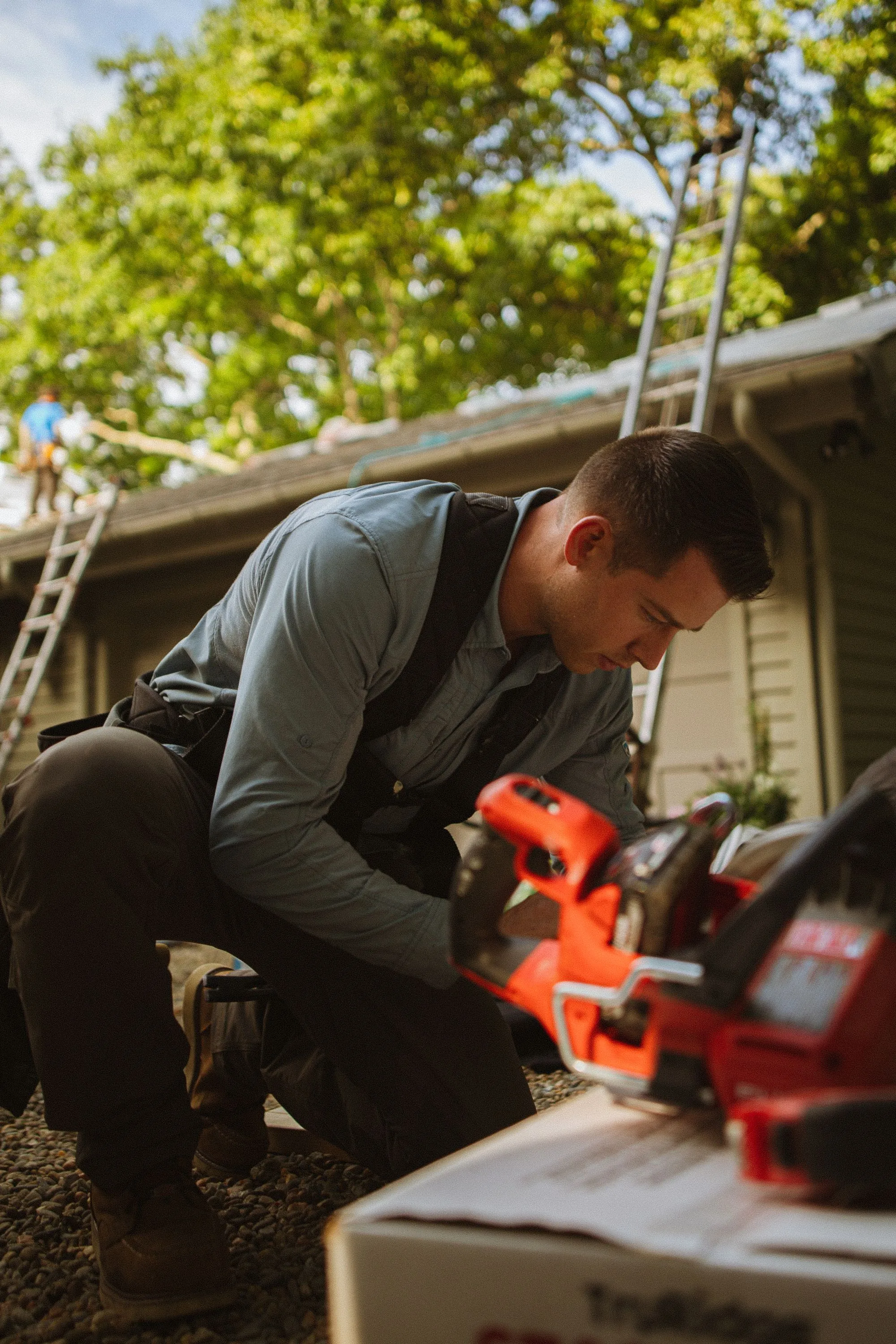 A roofer driving a fastener into new roof sheathing with a cordless drill