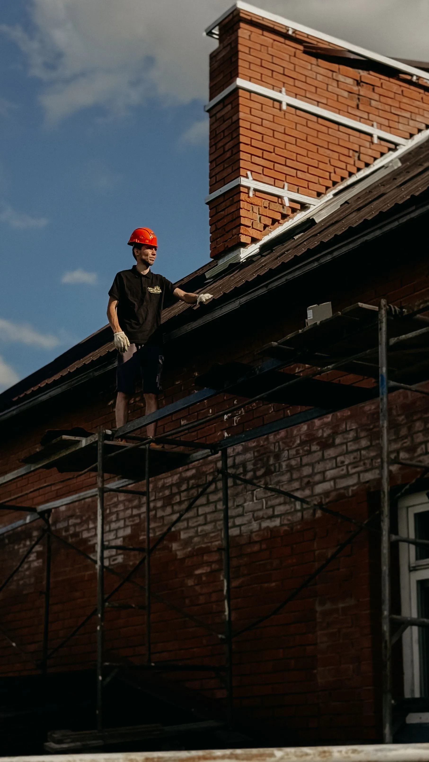 A roofer working along the edge of a residential roof from a scaffold