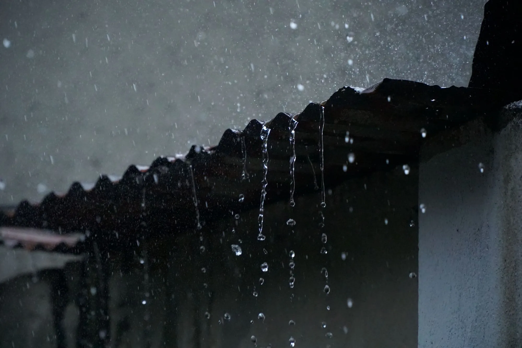 Rain pouring off the edge of a residential roof during a storm